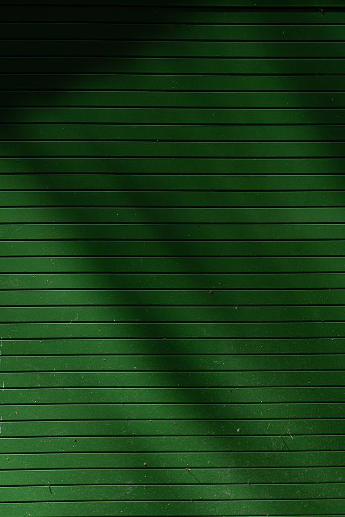 Abstract green metal wall with horizontal lines and shadow patterns creating texture.